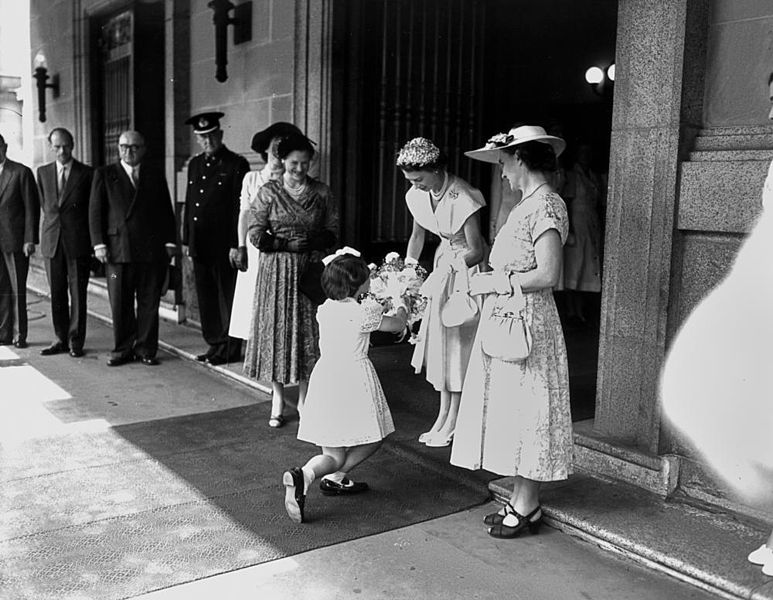 A young girl curtsies as she presents a bouquet of flowers to Queen Elizabeth II outside Brisbane City Hall in March 1954.